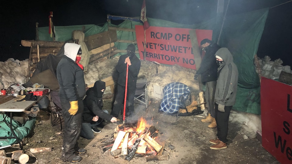 Cinq manifestants se réchauffent autour d'un feu de camp.