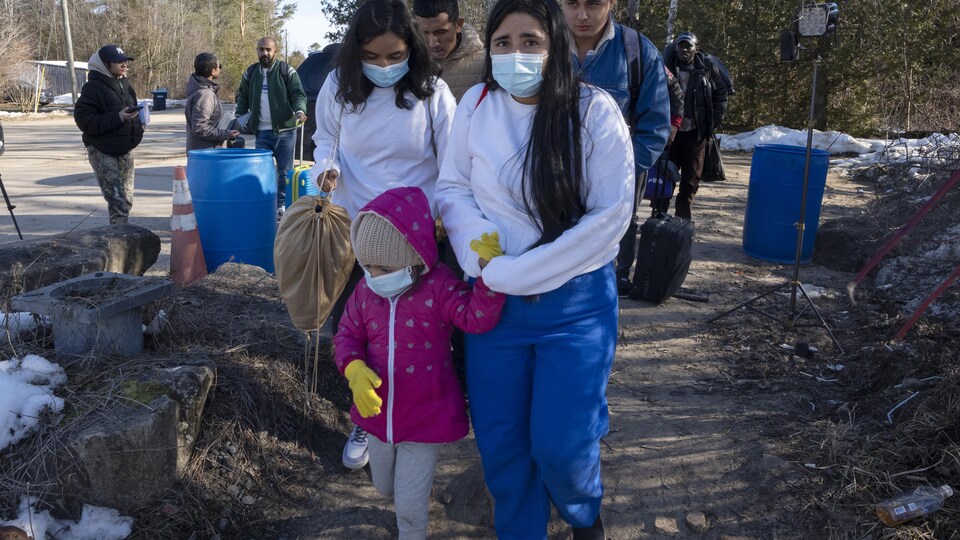 Une femme portant un masque chirurgical marche en tenant la main d'un enfant. D'autres personnes marchent derrière elle.