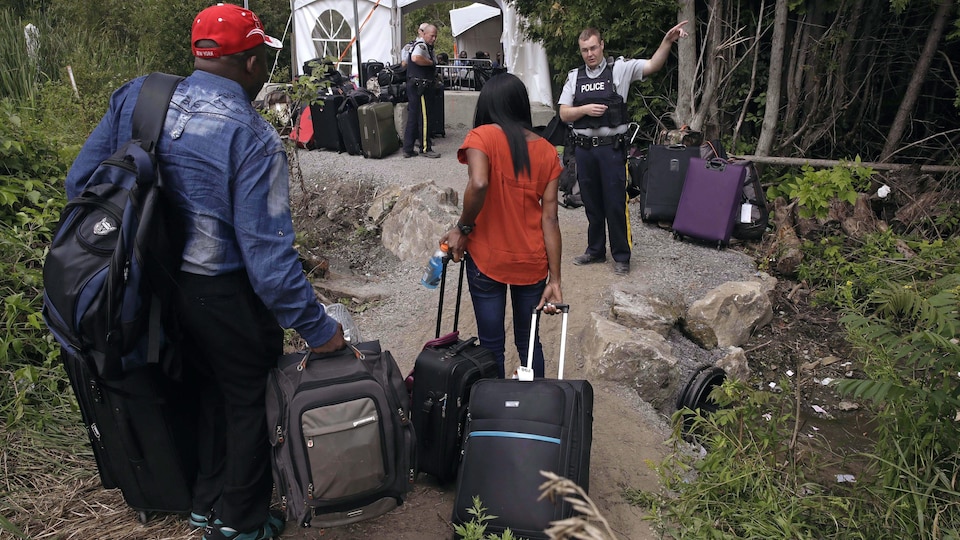 Les migrants marchent avec leurs valises dans un chemin caillouteux.