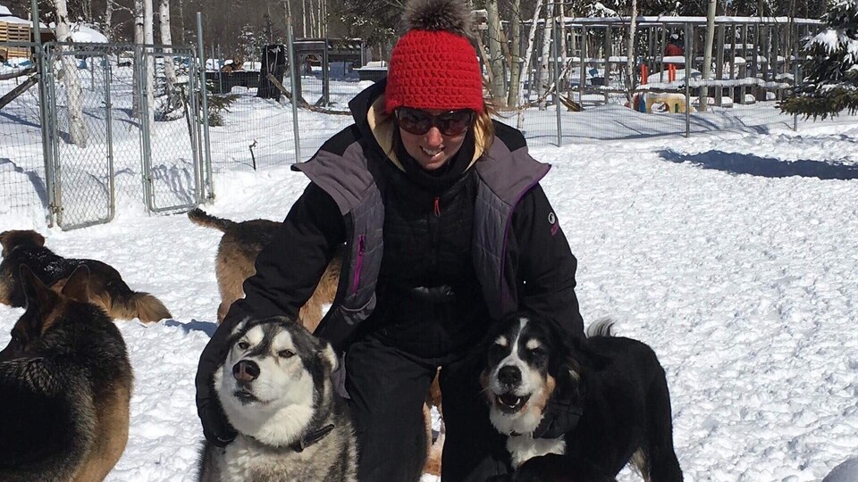 Une femme sourit en tenant deux chiens de chaque côté d'elle.