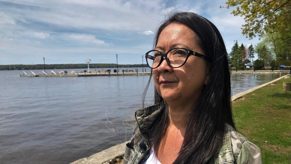 Une femme mohawk pourtant des lunettes est debout devant un quai à l'extérieur.