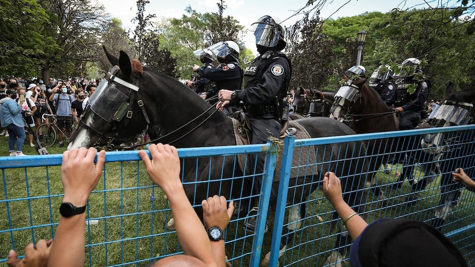 Des policiers à cheval près d'une clôture qui bloque des manifestants.
