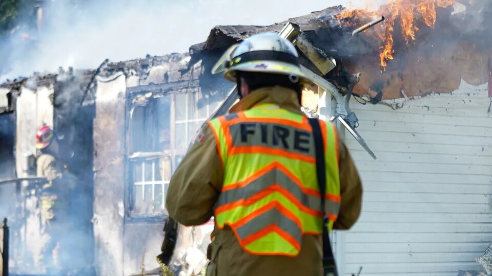 Des pompiers tentent d'éteindre le feu qui consume une maison.