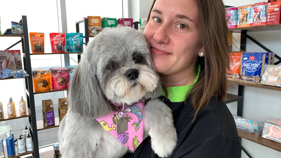 Natalie Ulaszonek tient un chien dans ses bras près de rayons de friandises pour animaux.