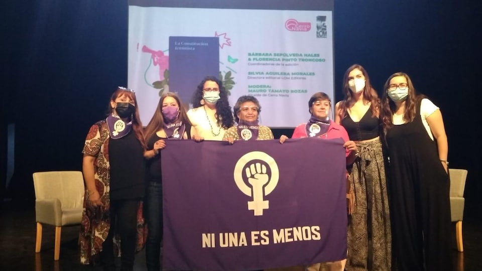 Sept femmes devant une affiche où est écrit le slogan féministe latino-américain « Ni una es menos » (Pas une de moins).
