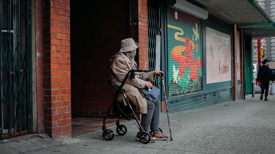An old man sits in a transport chair, in front of a mural painted on a building in Chinatown, Vancouver.