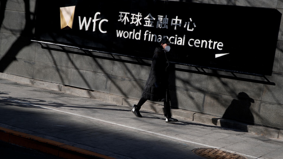 Une femme portant un masque passe devant un panneau indiquant World financial center.