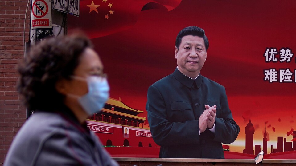 Une femme portant un masque protecteur aperçue dans une rue de Shanghai en passant devant un portrait géant du président chinois Xi Jinping. 