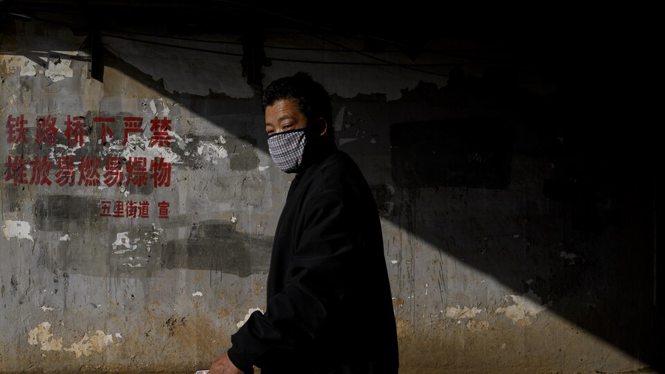 Un homme portant un masque sur la bouche marche dans la pénombre.