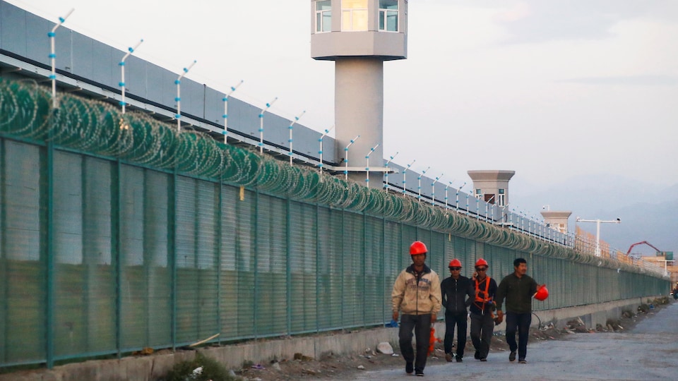 Des travailleurs chinois marchent le long d'une haute clôture ponctuée de mirador.