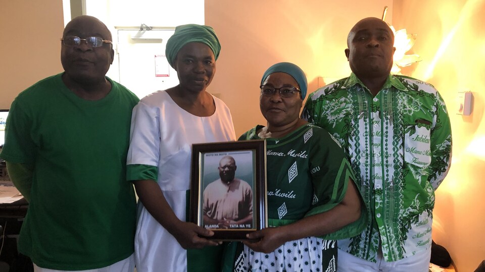 Quatre personnes habillées en vert. Deux d'entre elles tiennent un portrait.