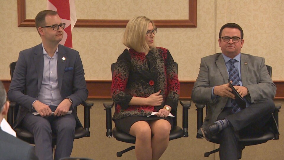 Trois personnes assises sur une estrade, lors d'une conférence dans un hôtel de Winnipeg.