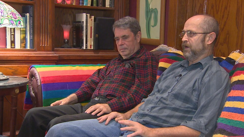 Deux hommes sont assis sur un divan côte à côte.