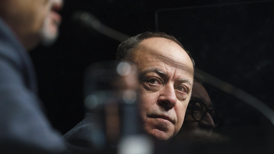 Gros plan de Christian Dubé et le reflet d'Horacio Arruda durant une conférence de presse.