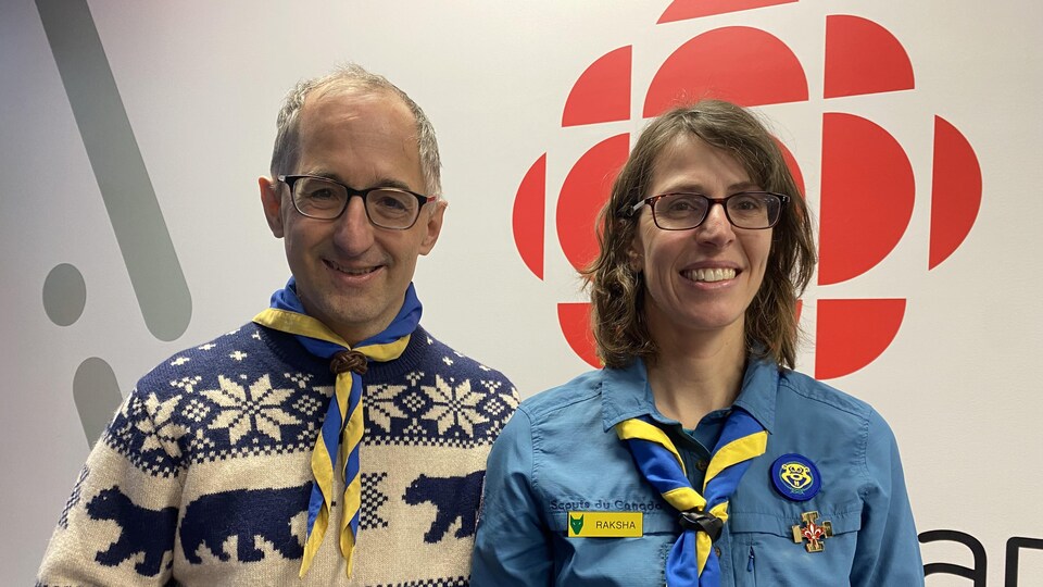 Christian Milot et Isabelle Castonguay dans les locaux de Radio-Canada. Ils portent tous les deux un foulard des scouts.