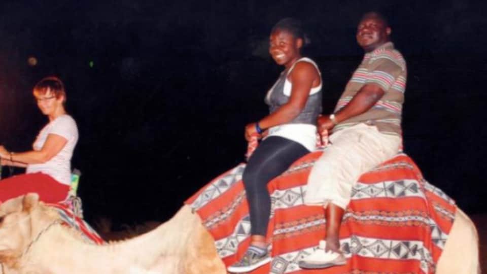 Christine Dikongué et son père sur le dos d'un chameau à côté d'une femme, elle aussi sur le dos d'un autre chameau.