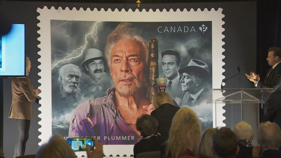 Le timbre en hommage à Christopher Plummer sur un grand écran est présenté à l'assemblée lors de la cérémonie en son honneur.