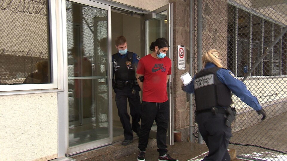 Un homme menotté est escorté par deux agents.