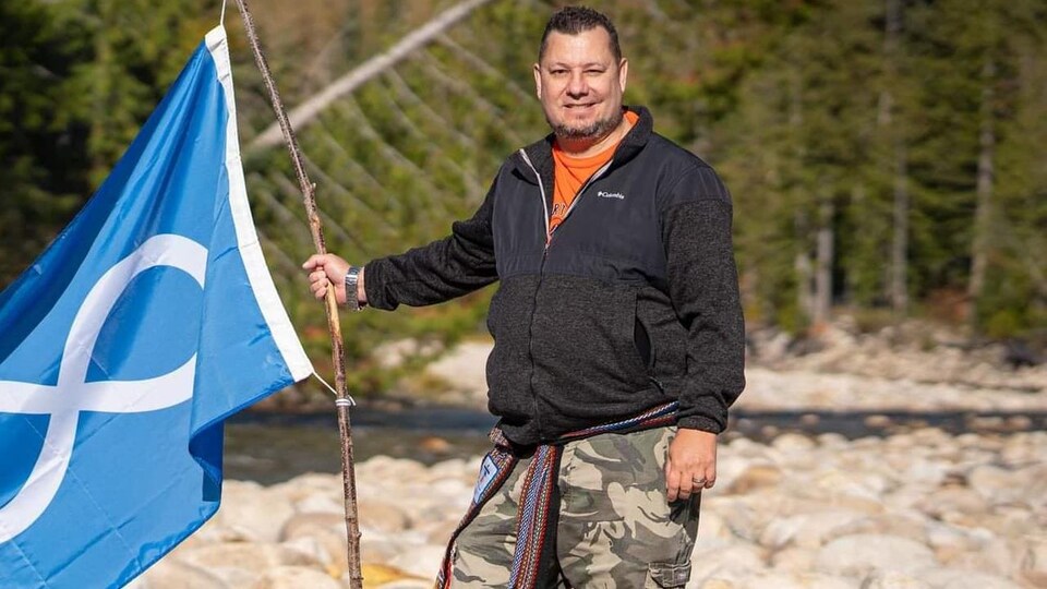 Christopher Yates, debout près d'une rivière, tient un drapeau métis, 