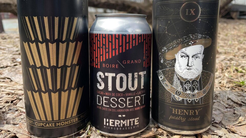 Trois cannettes de bière côte à côte posées sur le sol dehors.