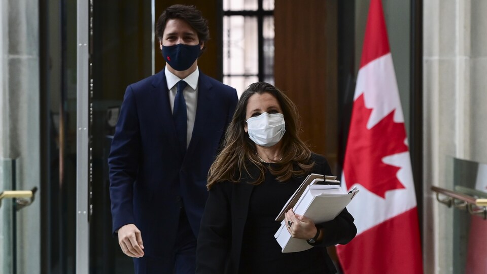 Chrystia Freeland, masquée, tenant des documents, marche, suivie de Justin Trudeau, également masqué.