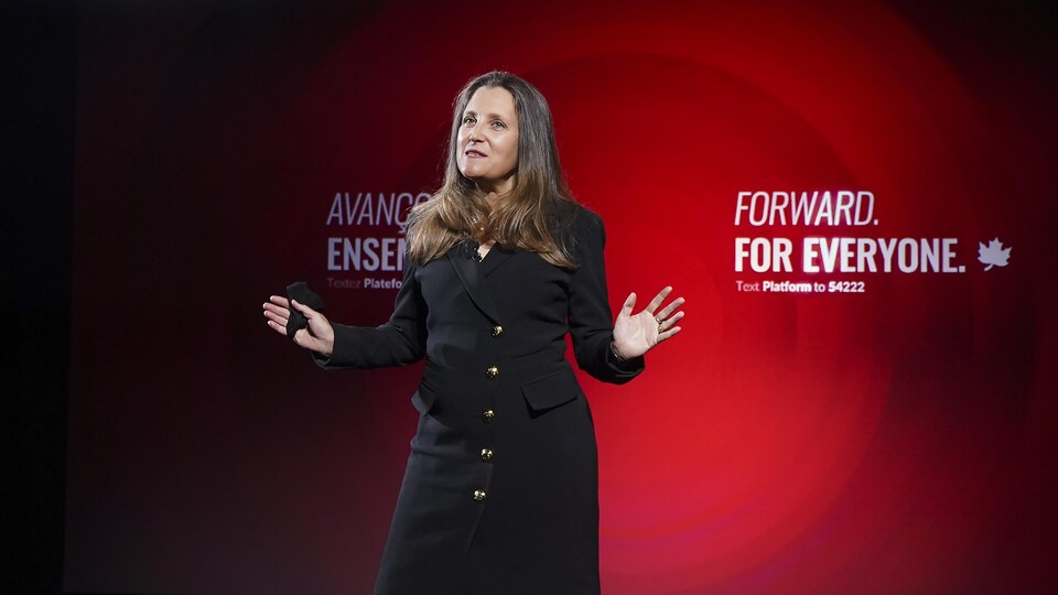 Chrystia Freeland parle devant un grand écran où est projeté le slogan du Parti libéral : « Avançons ensemble ».