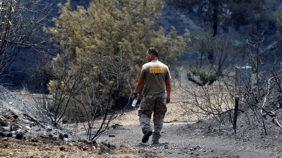 Un homme marche au milieu d'un paysage en cendres, une bouteille d'eau à la main.