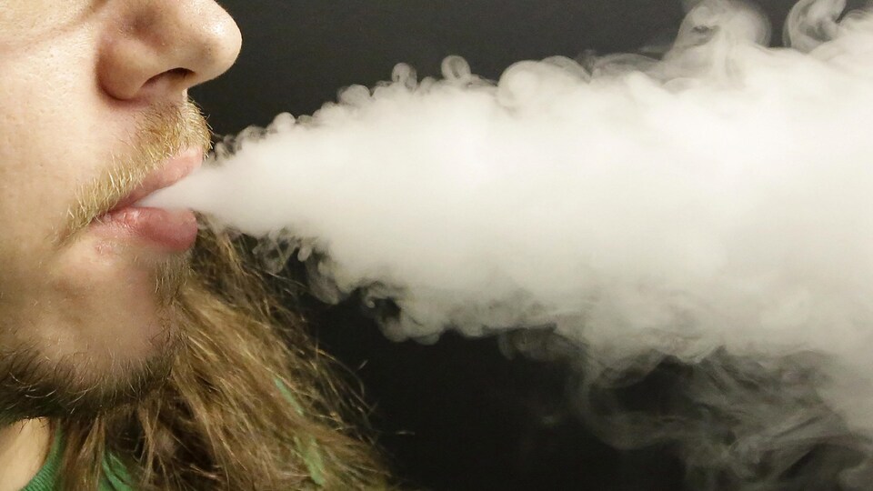 Un jeune homme fume une cigarette électronique.