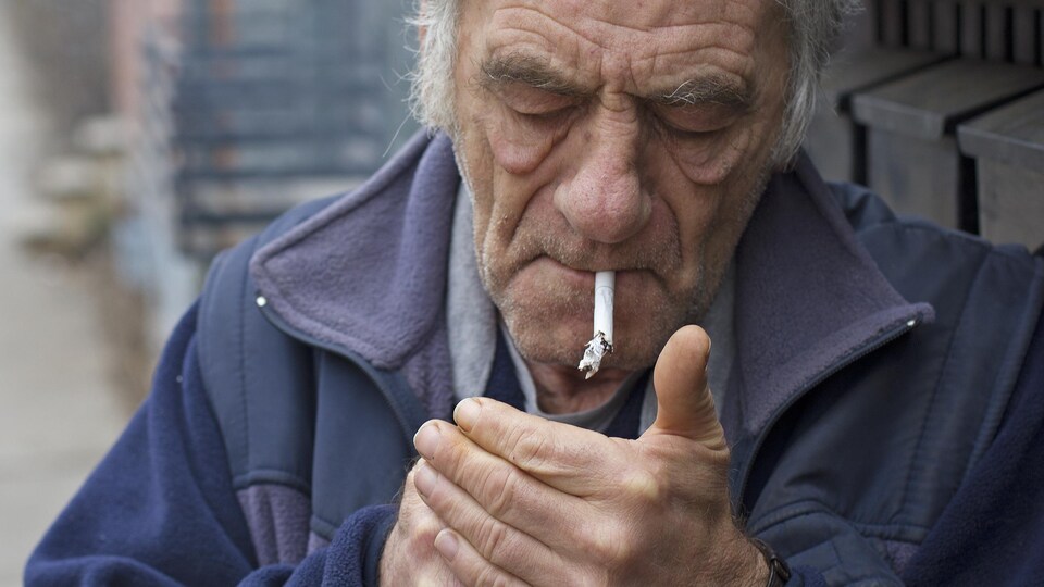 Homme âgé allumant une cigarette à l'extérieur.