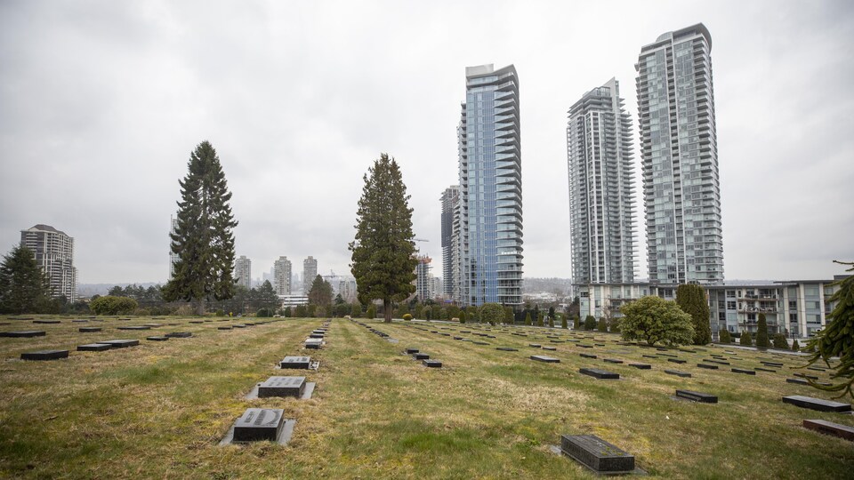 Des pierres tombales marquent des lieux de sépulture sur un terrain couvert d'herbe au pied de tours d'habitation.