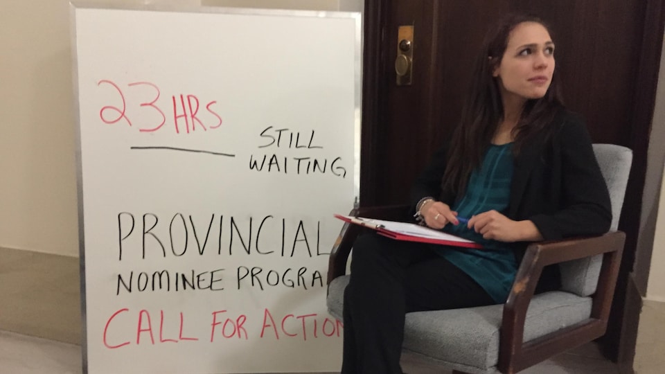 Une femme est assise devant la porte du bureau d'un ministre au palais législatif du Manitoba.