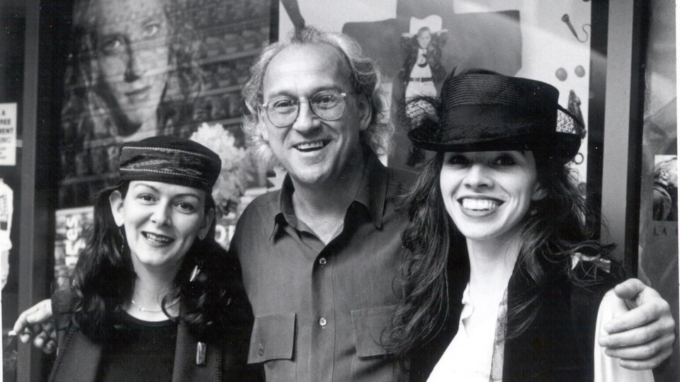 Photo en noir et blanc de deux femmes et d'un homme qui sourient. Les deux femmes portent un chapeau.