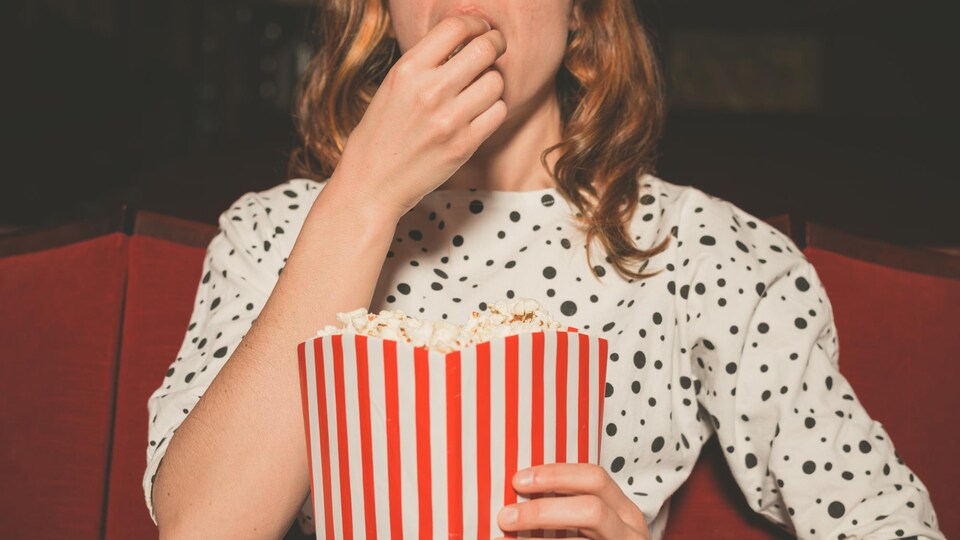 Une femme mange du maïs soufflé au cinéma.