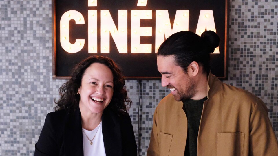 Une femme et un homme rient devant un panneau sur lequel est indiqué «cinéma».