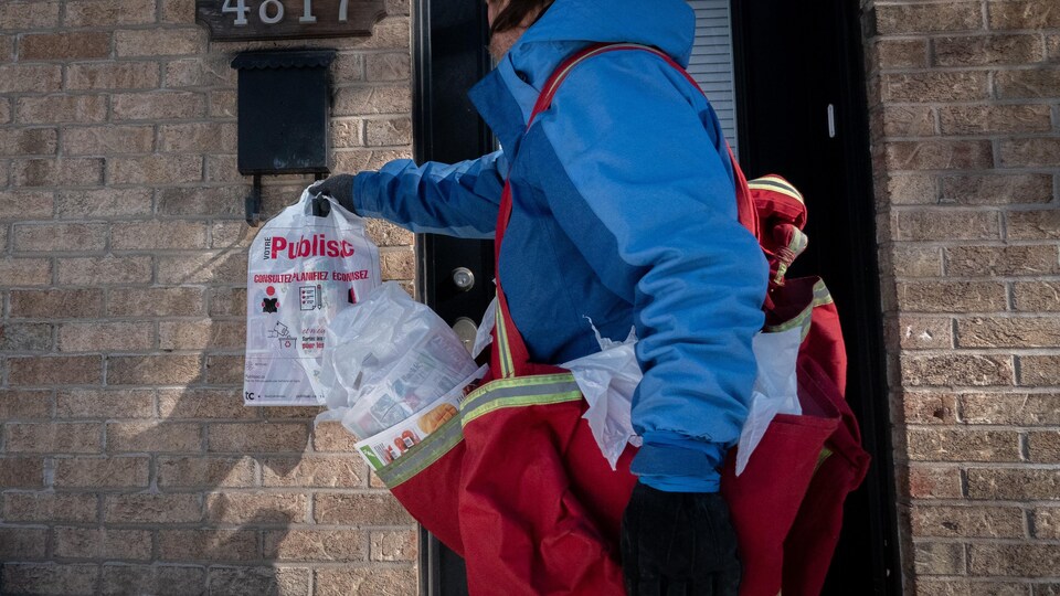 Un camelot accroche un Publisac à l'entrée d'une maison, à Montréal.