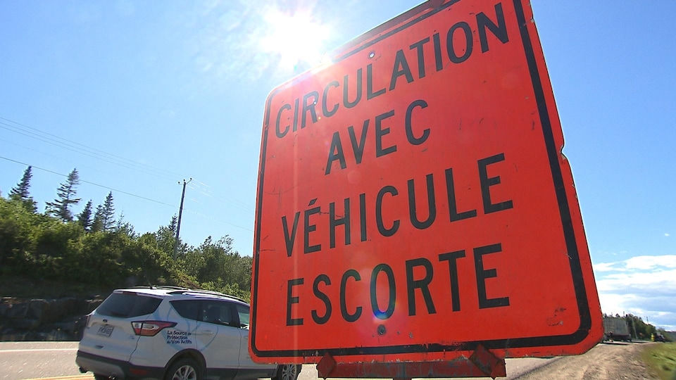 Un panneau de signalisation sur lequel il est écrit : circulation avec véhicule escorte. 