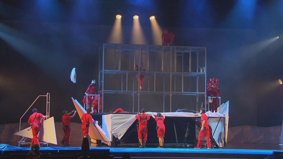 Une structure sur la scène et des gens de l'équipe technique ainsi que des acrobates.