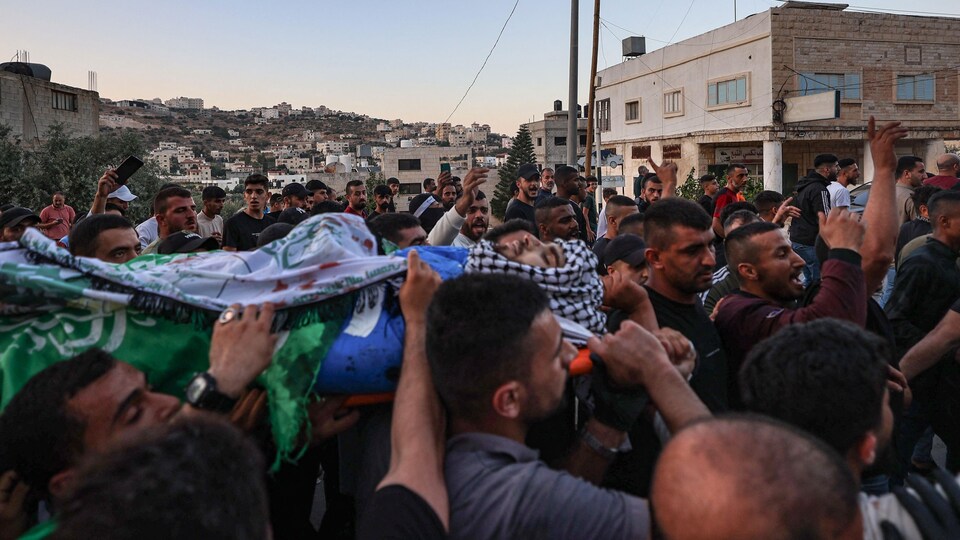 Une foule portant une dépouille lors de funérailles.