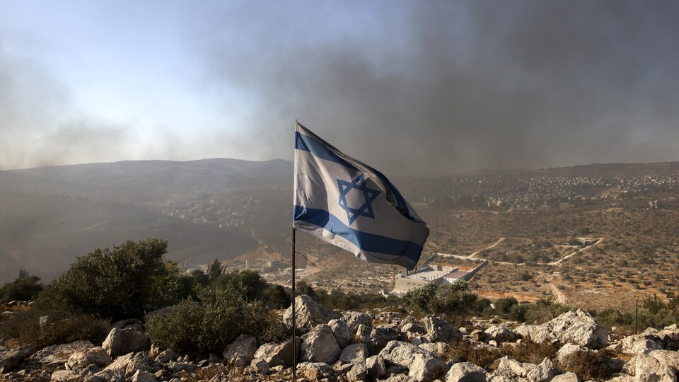 Un drapeau israélien planté sur une colline rocailleuse.