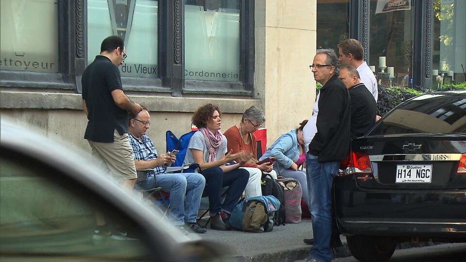 Des citoyens assis sur des chaises de camping sur un trottoir, à Montréal, devant un édifice.