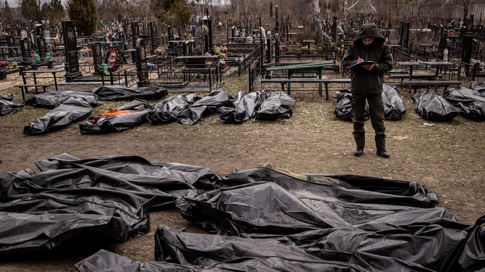 Un hombre toma notas cerca de varias bolsas para cadáveres que contienen cadáveres en un cementerio.