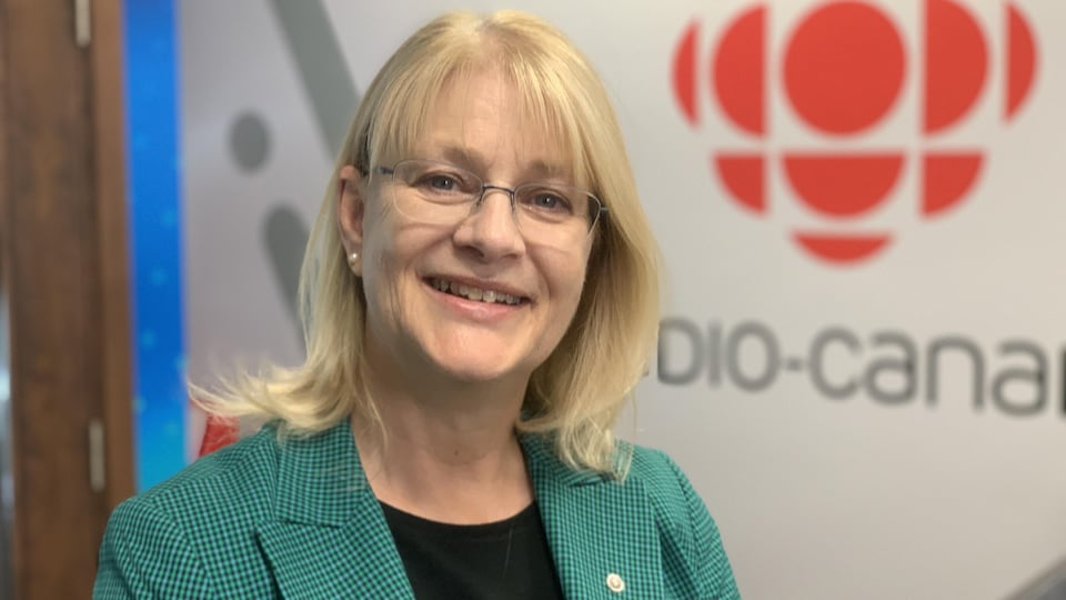 Claire Bolduc sourit à la caméra, le logo de Radio-Canada en arrière-plan.