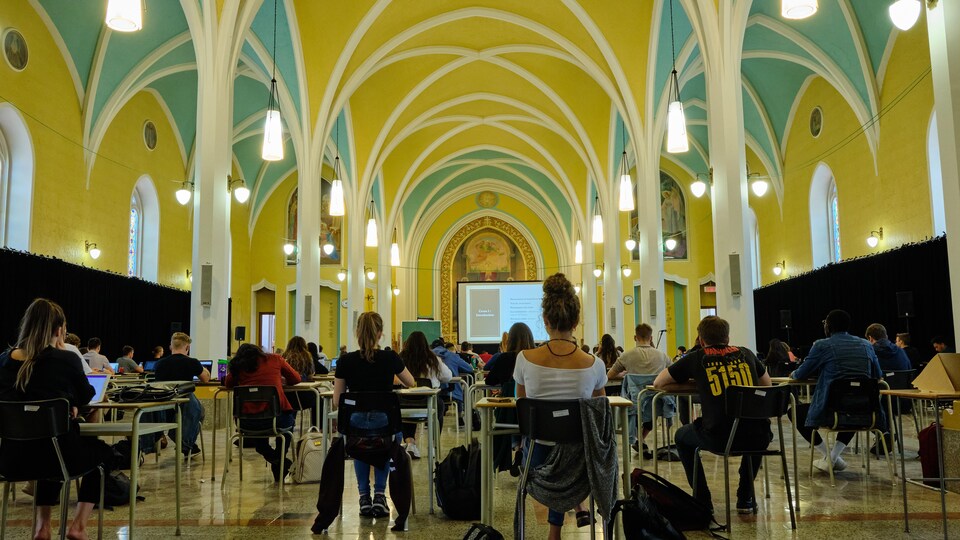 Les étudiants sont assis sur des pupitres installés dans la chapelle.