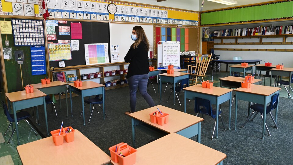 Une enseignante qui porte un couvre-visage se déplace dans une classe vide.