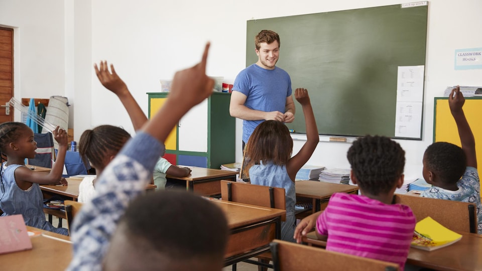 Des élèves noirs sont vus de dos dans une salle de classe, plusieurs lèvent la main.