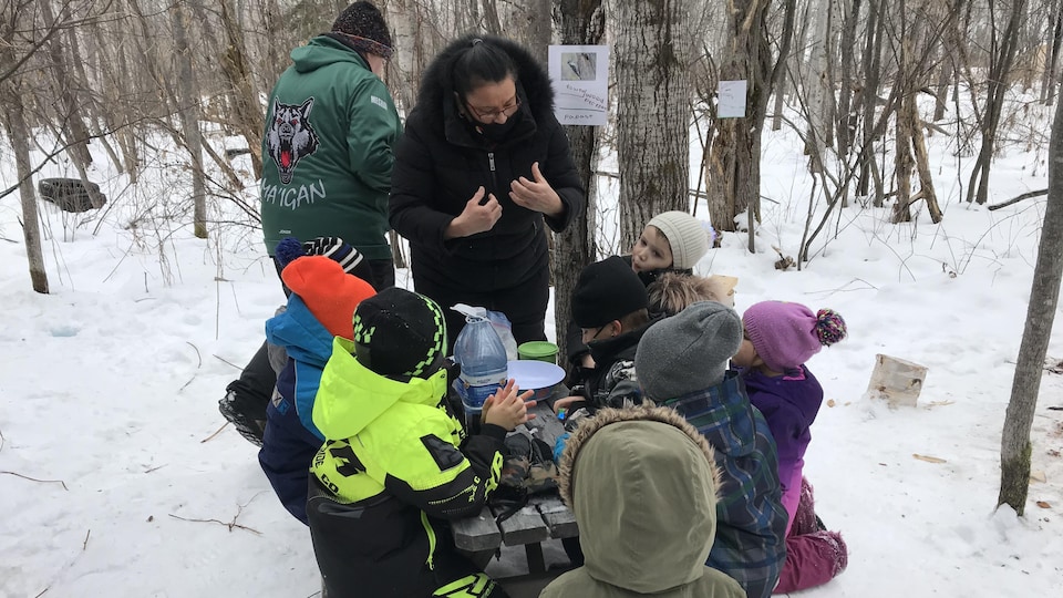 Une femme parle avec des enfants autour d'une table de pique-nique dans les bois.