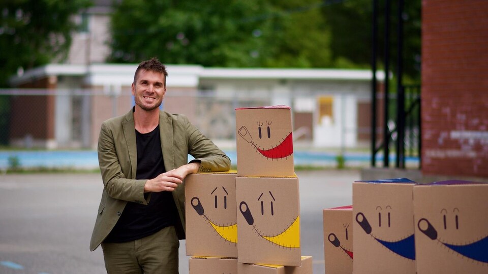 Daniel Quirion avec ses boîtes de carton sur lesquelles il y a un sourire de dessiné. 