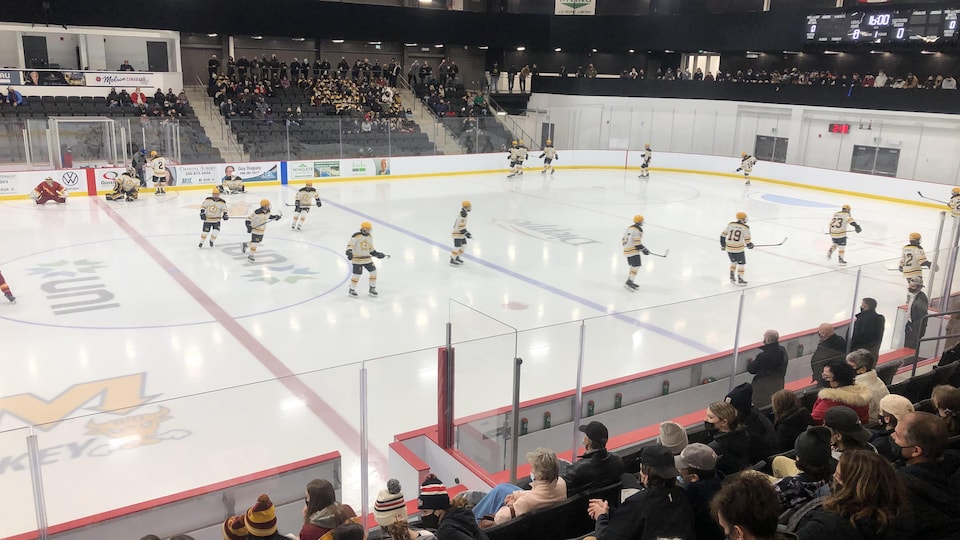Des joueurs de hockey sur la glace devant des spectateurs assis dans des gradins.