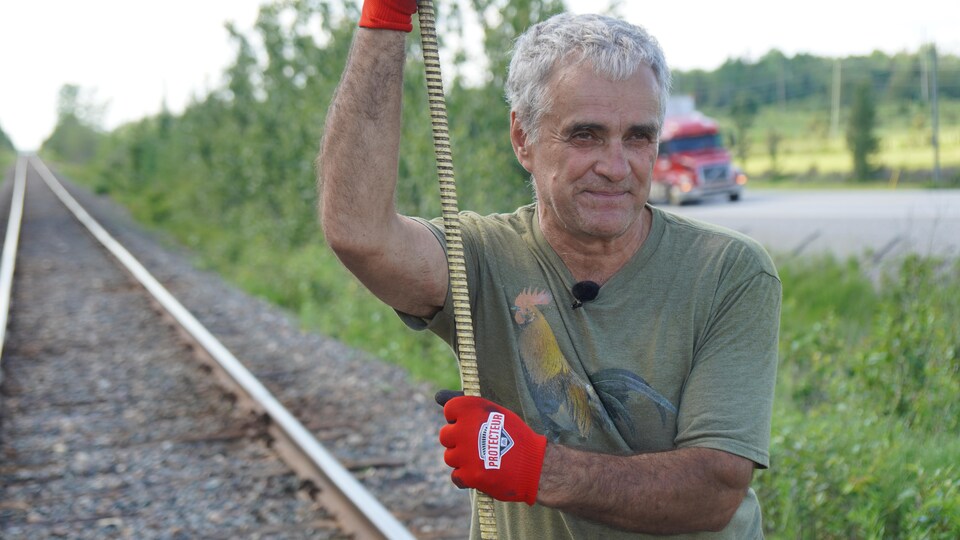 Un homme tient une longue tige de fer en bordure du chemin de fer.