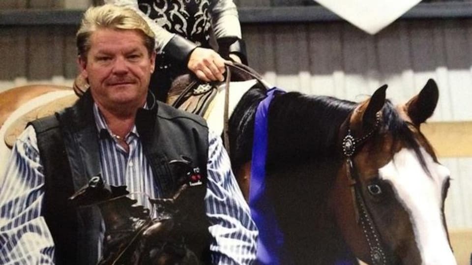 Un homme pose avec un trophée d'équitation, devant un cheval monté par une femme.